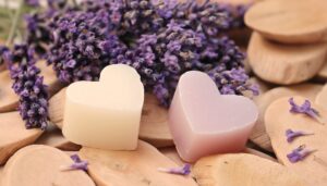 Heart-shaped lavender soaps on wooden surfaces with dried lavender flowers in the background.