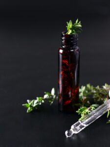 Amber bottle with thyme sprig and dropper on black background.