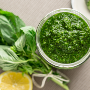 A jar of fresh basil pesto with basil leaves and a lemon half on the side.