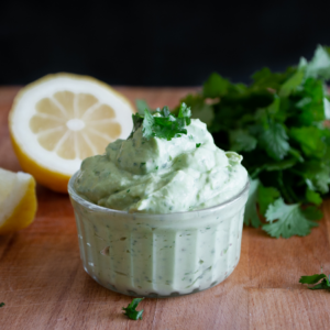 "Small bowl of creamy cilantro dip on a wooden board with a halved lemon and fresh cilantro in the background."