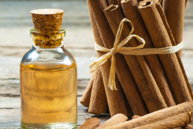 A bottle of cinnamon oil with a cork stopper placed next to a bundle of cinnamon sticks tied with twine, on a rustic wooden surface.