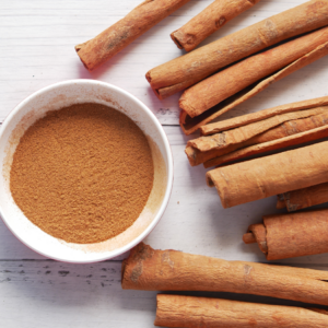 Article: How Can Cinnamon Control Blood Sugar Levels And Reduce Inflammation. A bowl of ground cinnamon placed next to several cinnamon sticks on a white wooden surface.