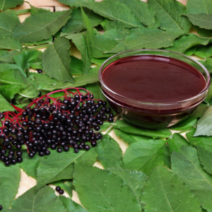 Article: Immune Boosting Elderberry Tea Benefits. Pic "Glass bowl of elderberry juice and a cluster of black elderberries on a bed of green leaves."