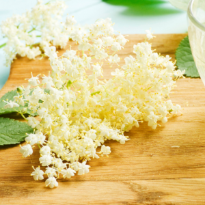 "Cluster of fresh white elderflowers on a wooden surface with green leaves in the background."