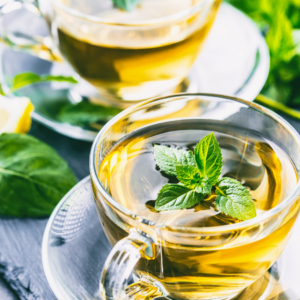 Article: Raspberry Leaf tea. Pic - A clear glass cup of golden raspberry leaf tea garnished with fresh mint leaves, set on a slate coaster.