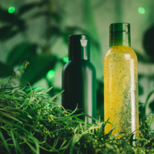 Two bottles of herbal products, one black and one clear with yellow liquid, surrounded by fresh tarragon leaves in a lush green setting.