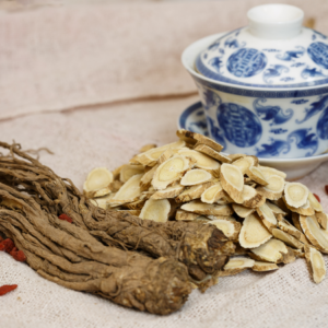 "Close-up of dried Angelica roots and sliced herbs next to a traditional blue and white porcelain tea cup."