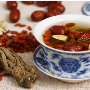 "Close-up of a traditional Chinese tea cup filled with herbal tea and various dried ingredients including Angelica root on a beige cloth background."