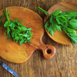 Fresh lovage leaves on wooden cutting boards with a knife on a rustic wooden table.