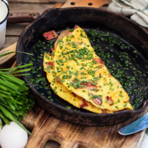  A close-up view of an omelet sprinkled with chopped chives, served in a cast-iron skillet with fresh chives and an egg nearby.