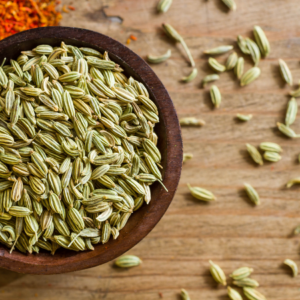 Article: fennel uses and benefits. Pic - A wooden bowl filled with fennel seeds on a rustic wooden table, with some seeds scattered around.