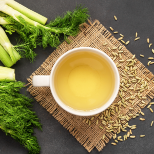 Article: fennel uses and benefits. Pic - A cup of fennel tea on a burlap mat, surrounded by fresh fennel fronds and scattered fennel seeds.