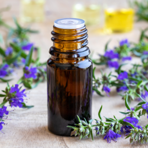 A small amber bottle of hyssop essential oil surrounded by fresh hyssop flowers with vibrant purple blooms.