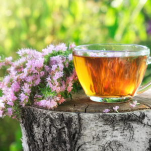 A glass cup of catnip tea placed on a rustic tree stump with blooming catnip flowers nearby, set against a vibrant outdoor background.