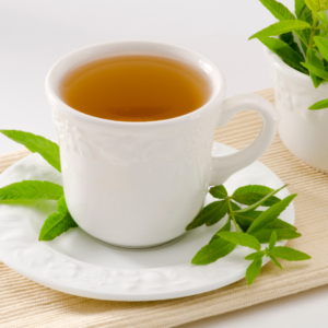  A white ceramic cup filled with herbal tea, garnished with fresh lemon verbena leaves, placed on a white saucer with a few leaves.