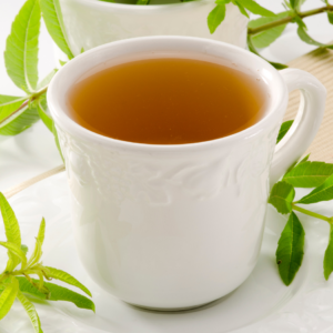  A white ceramic cup filled with herbal tea, garnished with fresh lemon verbena leaves, placed on a white saucer with lemon verbena leaves around it.