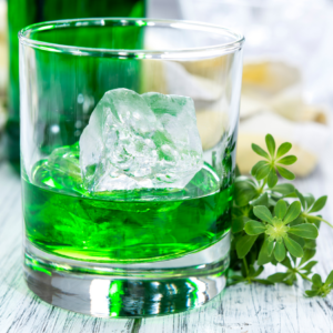 Green woodruff drink in a glass with ice, garnished with fresh woodruff sprigs.