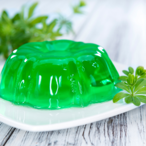 Green woodruff jelly on a white plate with fresh woodruff sprigs.