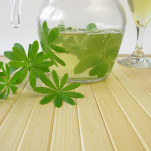 Woodruff-infused beverage in a glass pitcher with fresh woodruff leaves.