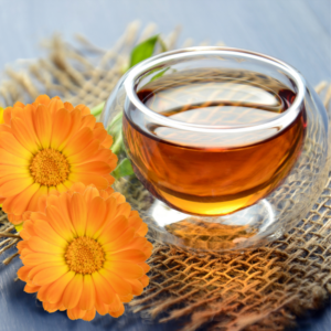 Glass cup of calendula tea with fresh calendula flowers.