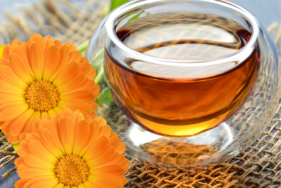 Glass cup of calendula tea with fresh calendula flowers.