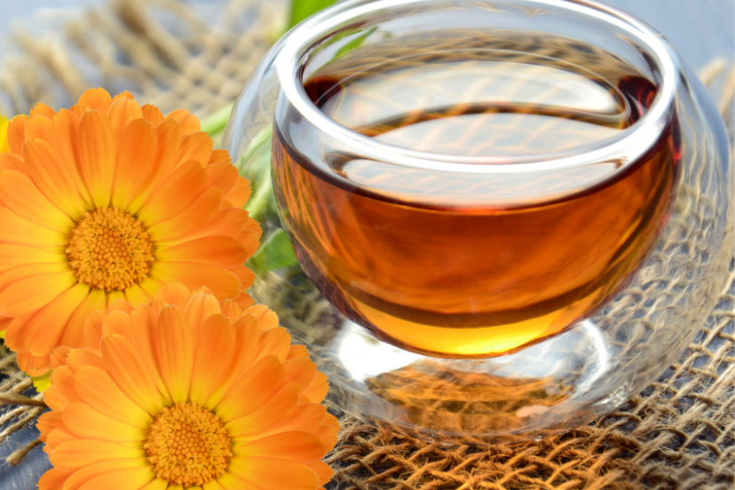 Glass cup of calendula tea with fresh calendula flowers.