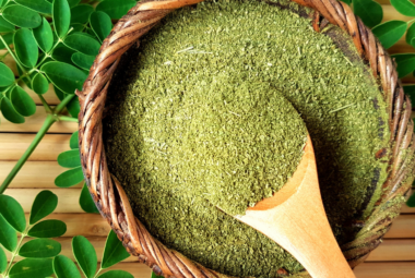 Bowl of moringa powder with fresh moringa leaves.