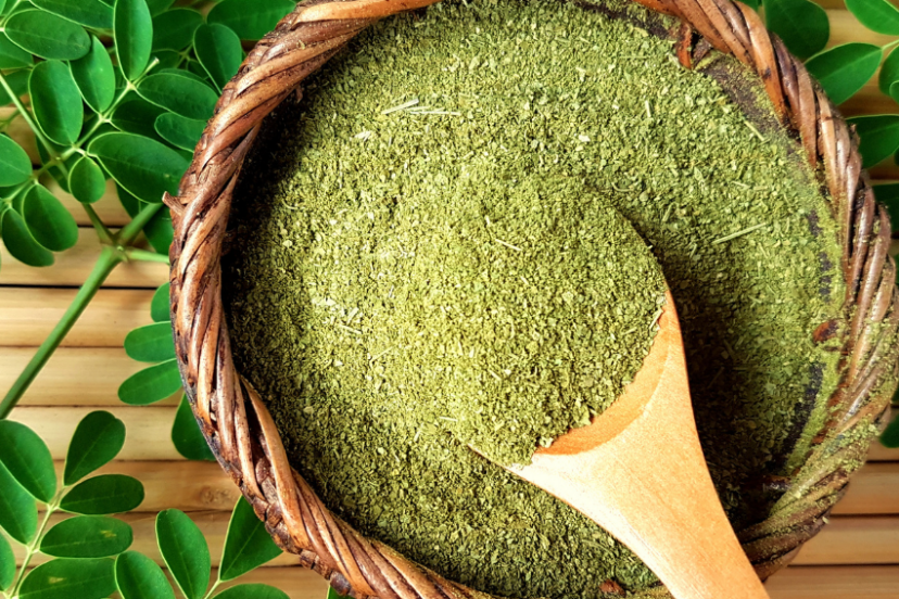 Bowl of moringa powder with fresh moringa leaves.