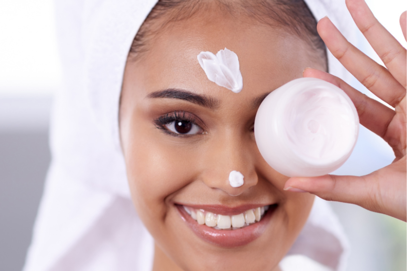 A smiling person with a towel on their head applies marshmallow root cream to their face while holding a jar.