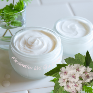 jars of creamy skincare product, surrounded by green leaves and marshmallow flowers.