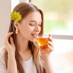 enjoying a cup of tea with a coltsfoot flower in her hair, sitting by a window.